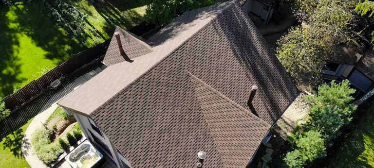 Person using a soft brush and garden hose to clean moss from a low-slope shingle roof safely.