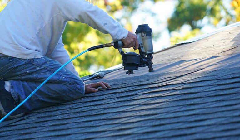 Homeowner inspecting roof shingles and flashing from the ground with binoculars and a flashlight.