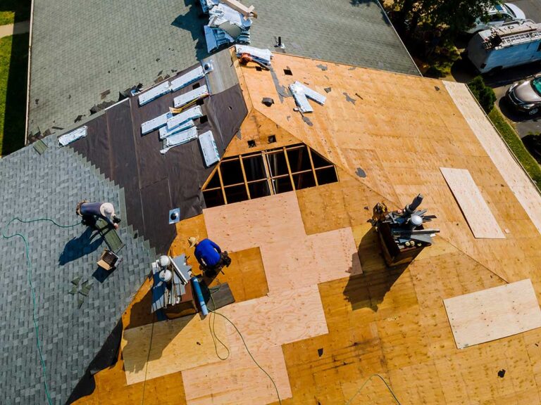 Homeowner examining shingles and gutters from the ground beside a snow-ready house.
